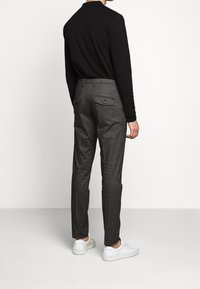 Pantaloni grigi su misura con una sottile texture, dotati di due tasche posteriori e una vestibilità slim. Indossati con una camicia nera a maniche lunghe e sneakers bianche.