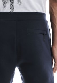 Marineblaue Jogginghosen aus weichem Material mit schlanker Passform, elastischem Bund und einer unauffälligen Reißverschlusstasche auf der Rückseite.