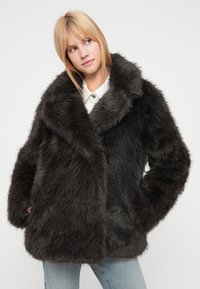 Παλτό από τεχνητή γούνα σε σκούρο γκρι, με φαρδιά γιακά, μεγάλη εφαρμογή και υφή στην επιφάνεια. Το μπουφάν διαθέτει πλαϊνές τσέπες και απαλό φινίρισμα.