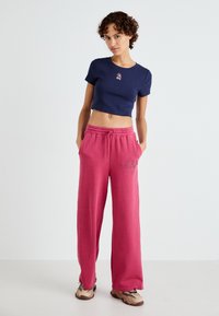 T-shirt navy court avec un petit design brodé, associé à un pantalon de survêtement rose ample avec un logo près de la taille.