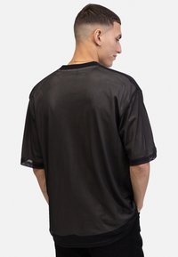 Sort mesh t-shirt med korte ærmer, løs pasform, rund halsudskæring og subtilt tekstureret mønster, der viser en afslappet silhuet fra ryggen.
