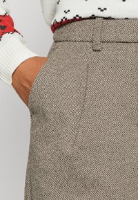 Spodnie w szary deseń hounds-tooth o gładkiej fakturze, z jedną kieszenią i prostym stanem, w połączeniu z białym swetrem z dzianiny.