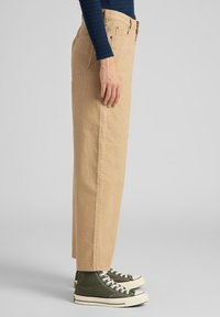 Beiga kordflanellbyxor med rak passform, sidofickor och ton-i-ton sömmar, matchade med gröna högstövlar med vita sulor.