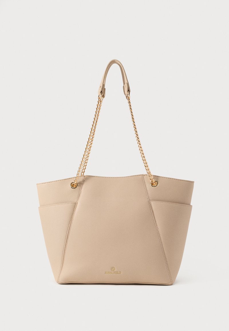 Sac fourre-tout en cuir beige avec une forme structurée, doté de bandoulières en chaîne dorée et de poches latérales discrètes ; logo de la marque embossé à la base.