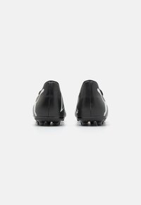 Botas de fútbol negras con un acabado texturizado, que presentan acentos blancos y una silueta alargada, diseñadas para proporcionar tracción con tacos moldeados.