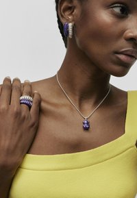 Joyería morada y plateada: un par de pendientes de aro, un anillo con bandas superpuestas y un collar con un colgante morado, todos combinados con una blusa amarilla.