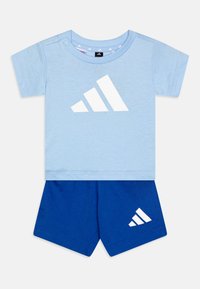 Camiseta de algodón azul clara con logo blanco de Adidas, combinada con pantalones cortos de algodón azules que tienen un pequeño logo blanco de Adidas en el costado.