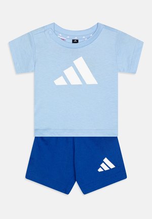 Lysblå bomulds-t-shirt med hvid Adidas-logo, parret med blå bomulds-shorts med et lille hvidt Adidas-logo på siden.