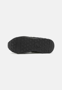 Sole in gomma nera per sneakers, con punti testurizzati, brand embossato e una frase incisa. Forma piatta e arrotondata con un design robusto.