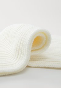 Un tessuto bianco a maglia arrotolato in una morbida curva, caratterizzato da un motivo a costine testurizzato e da una finitura liscia e raffinata.