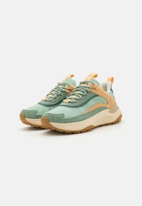 Mint green and beige sneakers featuring a mesh upper, suede accents, textured sole, and orange laces with pull tabs for easy wear.