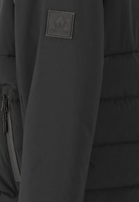 Zwarte gewatteerde jas met een ritszak en een gevoerde, matte logopatch met bergontwerp op de bovenarm.
