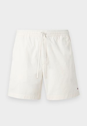 Hvite shorts med elastisk midje og snor, med liten Tommy Hilfiger-logo nær kanten på venstre ben mot enkel bakgrunn.