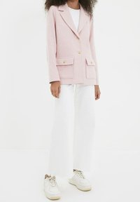 Blazer rose texturé avec des boutons dorés, deux poches avant, associé à un pantalon large blanc et des baskets blanches.