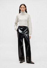 Camisola de gola alta cinza clara com côrte canelado, design curto; combinada com calças pretas de vinil brilhante e cintura alta. Sapatos pretos de calçar com tachas.