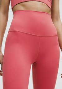 Hooggetailleerde legging in een effen koraalroze kleur. Gemaakt van rekbare, gladde stof. Voorzien van platte naden voor comfort en een strakke uitstraling.