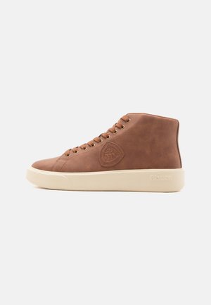 Bruine hoge sneaker met een beige rubberen zool, bruine veters en een reliëflogo op de zijkant, geplaatst tegen een eenvoudige lichte achtergrond.