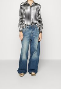 Person som bär en blus med svarta och vita vertikala ränder, urblekta vida blå jeans och metalliska guldfärgade ballerinaskor med rosetter.