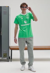 Zöld atlétikai trikó fehér díszítéssel, "Snapdragon" logóval. Szürke melegítőnadrággal, fehér tornacipővel és napszemüveggel kombinálva.