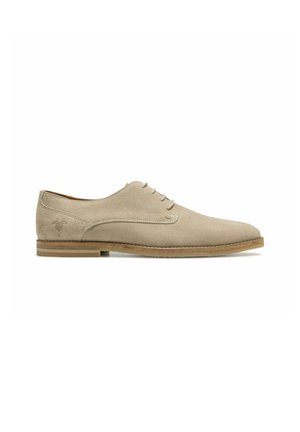 Chaussure Oxford en daim beige pour homme, avec laçage fermé, semelle fine et logo embossé discret près du talon, vue de profil.