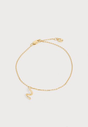 Delicato braccialetto con catena d'oro con un piccolo ciondolo astratto ondulato e chiusura a moschettone su uno sfondo chiaro e semplice.
