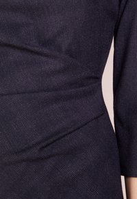 Robe bleu marine avec un tissu texturé à drapé diagonal, des manches trois-quarts et une silhouette ajustée.