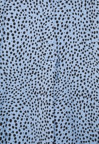 Tessuto blu con un motivo di punti neri sparsi. La superficie è liscia con una leggera lucentezza e i punti variano in dimensione e forma.