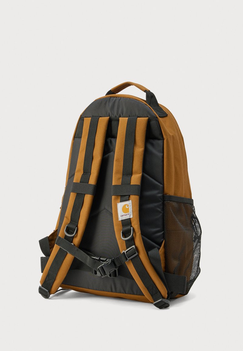 Sac à dos marron et noir avec un design rembourré, des bretelles ajustables, deux poches latérales en mesh et un patch logo à l'avant.