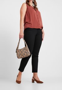 Roestkleurige mouwloze blouse met knopen, zwarte strakke broek, bruine blokhak schoenen en een lichtbruine handtas met slangpatroon.