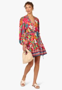 Rotes Kleid mit Blumenmuster, Puffärmeln, V-Ausschnitt und tailliert. Kombiniert mit einer beigen Handtasche und Sandalen.