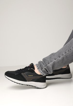 Zwarte en grijze sportieve schoenen met een bovenkant van suede en textiel, met een gevoerde zool en een logo aan de zijkant. Draag ze met grijze jeans.