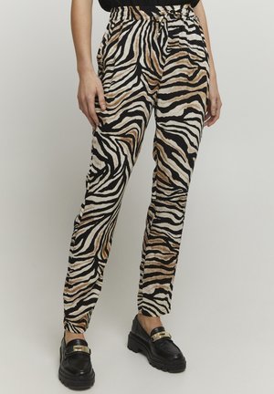 Persona con pantalones sueltos a rayas de cebra en negro, marrón y blanco combinados con mocasines negros gruesos.