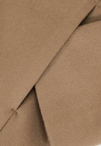 Pruun villane riie pehme tekstuuriga, millel on kaks kattuvat sektsiooni, igaühel on puhas serv ja peened kiudude detailid.