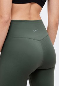 Gros plan d'une personne portant des leggings Nike vert foncé taille haute et un crop top noir, montrant le bas du dos et le haut des jambes.