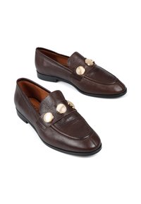 Brązowe skórzane mokasyny o gładkiej fakturze, z ostro zakończonym nosem i dwoma okrągłymi złotymi akcentami na cholewce. Niski obcas.