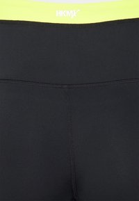 Svarta tights med ett brett midjeband i neonlysan. Har en slät textur och platta sömmar. Logotyp synlig på midjebandet.