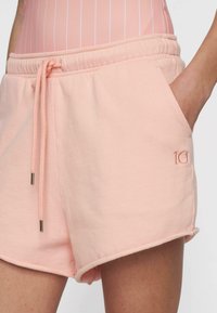 Pantalones cortos de color durazno con cinturilla elástica y cordón. Presenta un logo bordado de "10", bolsillos laterales y una textura suave.