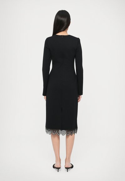 Fekete ruha hosszú ujjakkal, testhez simuló sziluettel, csipkés szegélydísszel. Kulcslyuk hátsó záródás és oldalsó hasítás a szegélyén.