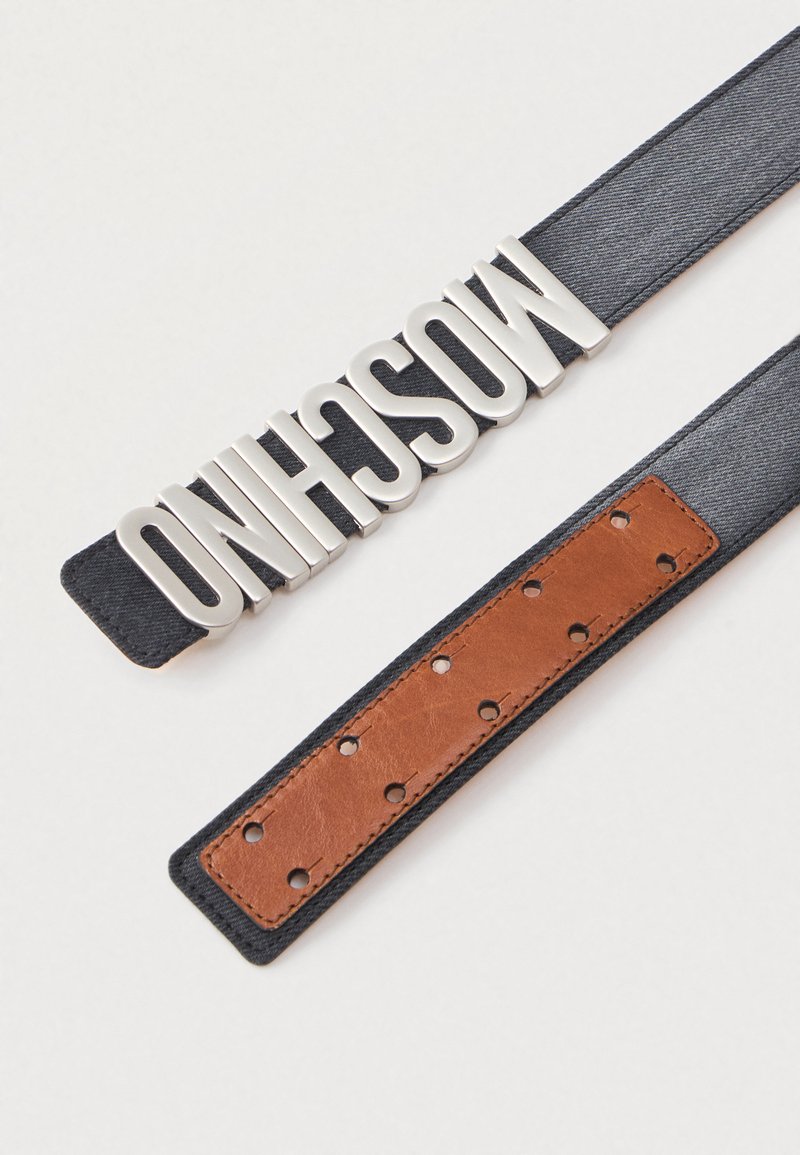 Cintura in denim grigio con lettere argentate che formano la parola "MOSCHINO" e una sezione in pelle marrone con fori perforati per la regolazione.