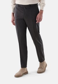 Dunkelgraue maßgeschneiderte Hose aus strukturiertem Stoff, mit einem Gürtelloops Bund und Seitentaschen, kombiniert mit beigen Knöchelstiefeln.