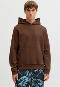 Hoodie marron en tissu doux, avec une grande capuche, une poche kangourou et un petit logo noir sur la poitrine.