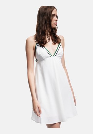 Vestido blanco sin mangas con escote en V, con rayas diagonales verdes y negras. Tejido ligero, corte holgado, textura suave, longitud a mitad del muslo.