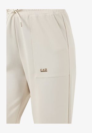 Pantaloni jogger beige realizzati in un tessuto morbido e liscio. Presentano un elastico in vita con cordino, tasche laterali e un piccolo logo dorato "EAZ" sulla tasca.