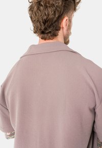 Übergröße, helllila Jacke aus strukturiertem Stoff, mit einem eingekerbten Kragen und kurzen Ärmeln. Die Rückansicht zeigt eine lockere Passform und Nahtdetails.