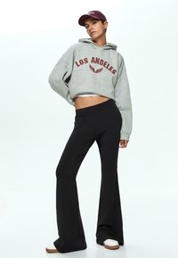 Gray cropped hoodie with "LOS ANGELES" print in burgundy, paired with black flared pants and white sneakers with brown soles.