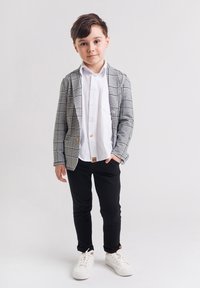 Szary w kratkę żakiet noszony na białej koszuli, czarnych spodniach i białych trampkach. Żakiet ma kieszeń oraz drewniany guzik.