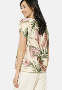 Blusa floreale in tessuto crema chiaro con motivi di foglie rosa e verdi, maniche corte con dettagli arricciati e un design svasato.