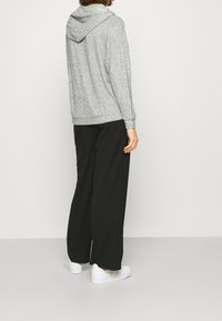 Grauer Hoodie mit weicher Textur, ausgestattet mit einer Kapuze, gerippten Bündchen und Saum. Kombiniert mit lockeren schwarzen Hosen und weißen Sneakers.