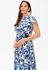 Robe portefeuille florale en crème avec de grands motifs bleus. Elle dispose de manches courtes, d'un lien à la taille et d'un ourlet évasé.