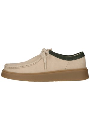 Beige casual schoen van suède met een groene leren kraag, ronde neus, vetersluiting aan de voorkant en dikke bruine rubberen zool.